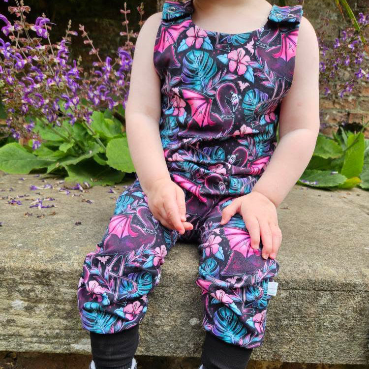 Child wearing a colorful floral outfit sitting on a stone ledge with flowers in the background
