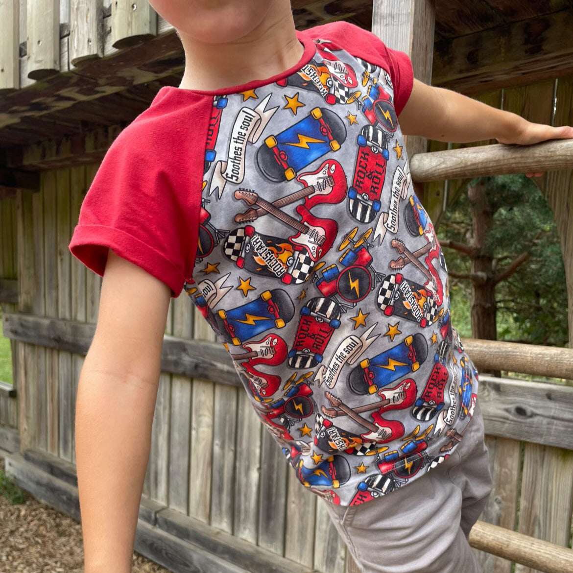 a colorful graphic t-shirt with red sleeves, standing outdoors near a wooden fence.