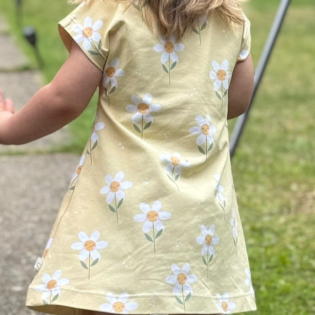 Child wearing a yellow dress with daisy pattern outdoors