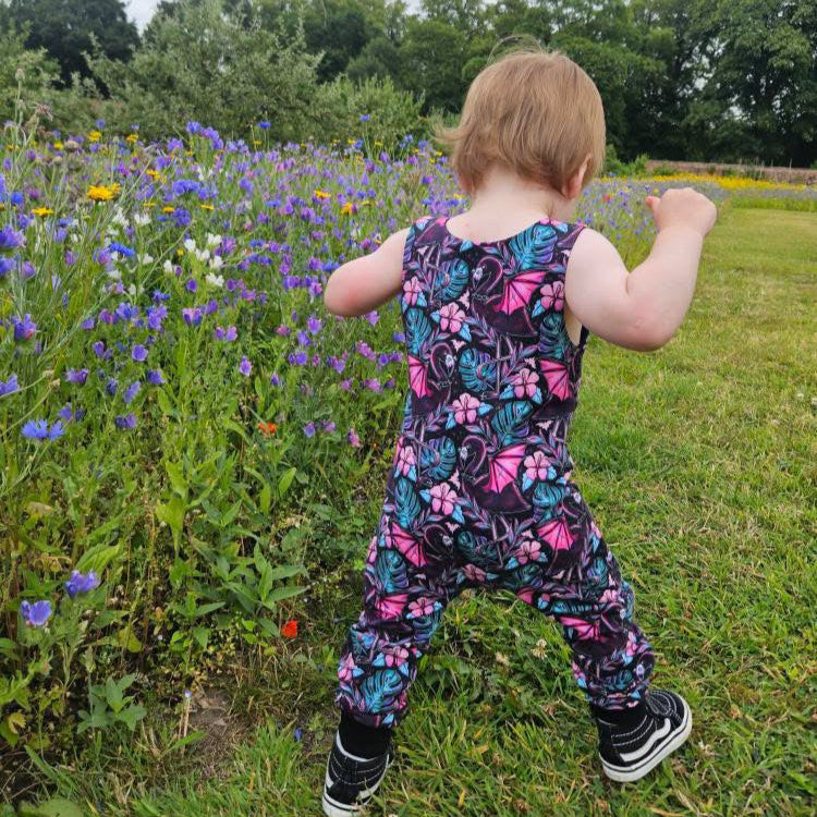 Child in a colorful floral outfit standing in a field of flowers with trees in the background