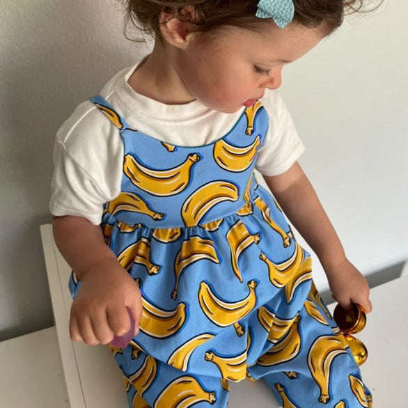 Child wearing a blue romper with yellow banana pattern and a white shirt underneath.