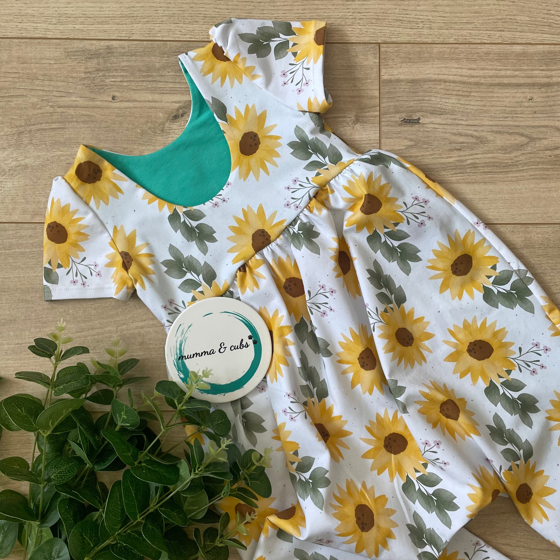 Romper with sunflower pattern on a wooden floor with a plant.