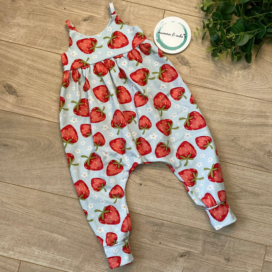 A long leg bubble romper for babies, with a pattern of strawberries and leaves on a blue background, displayed on a flat surface.
