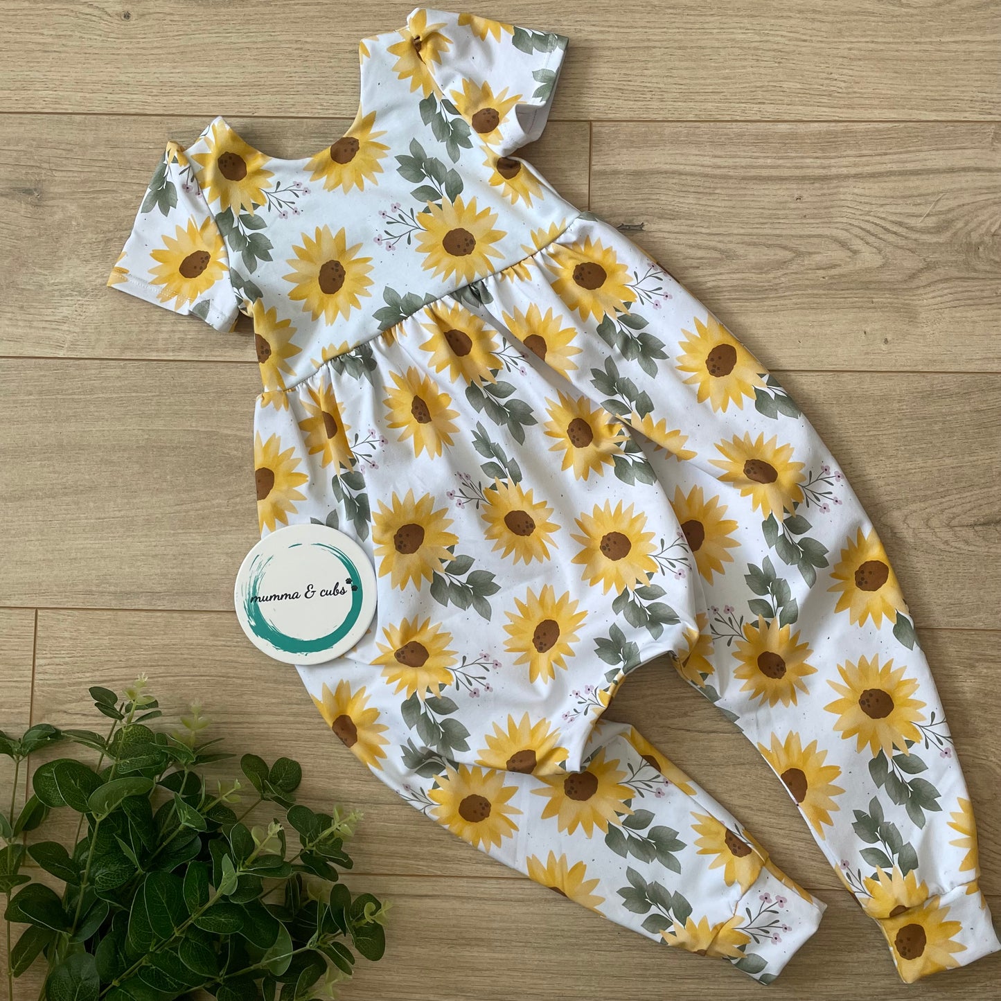 Sunflower-patterned childs bubble romper outfit on a wooden floor with a plant.