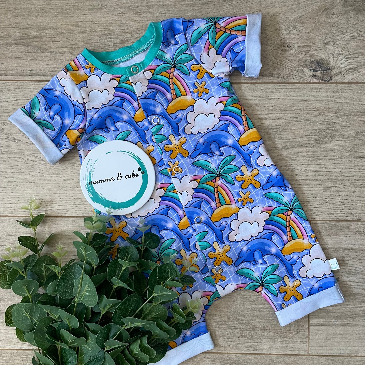 Colourful short romper for babies. With dolphins and palm trees with rainbows on a swimming pool background 