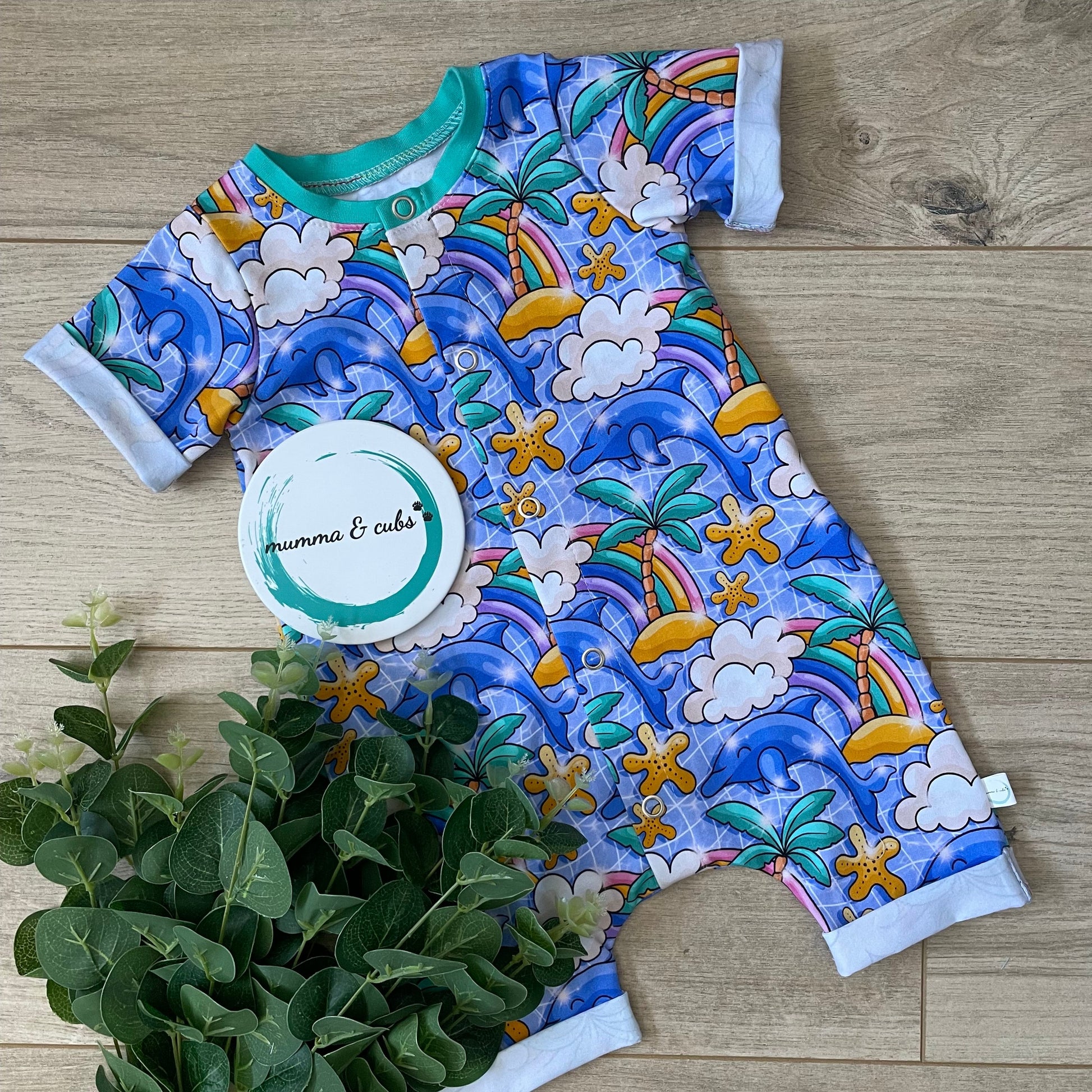 Colourful short romper for babies. With dolphins and palm trees with rainbows on a swimming pool background 