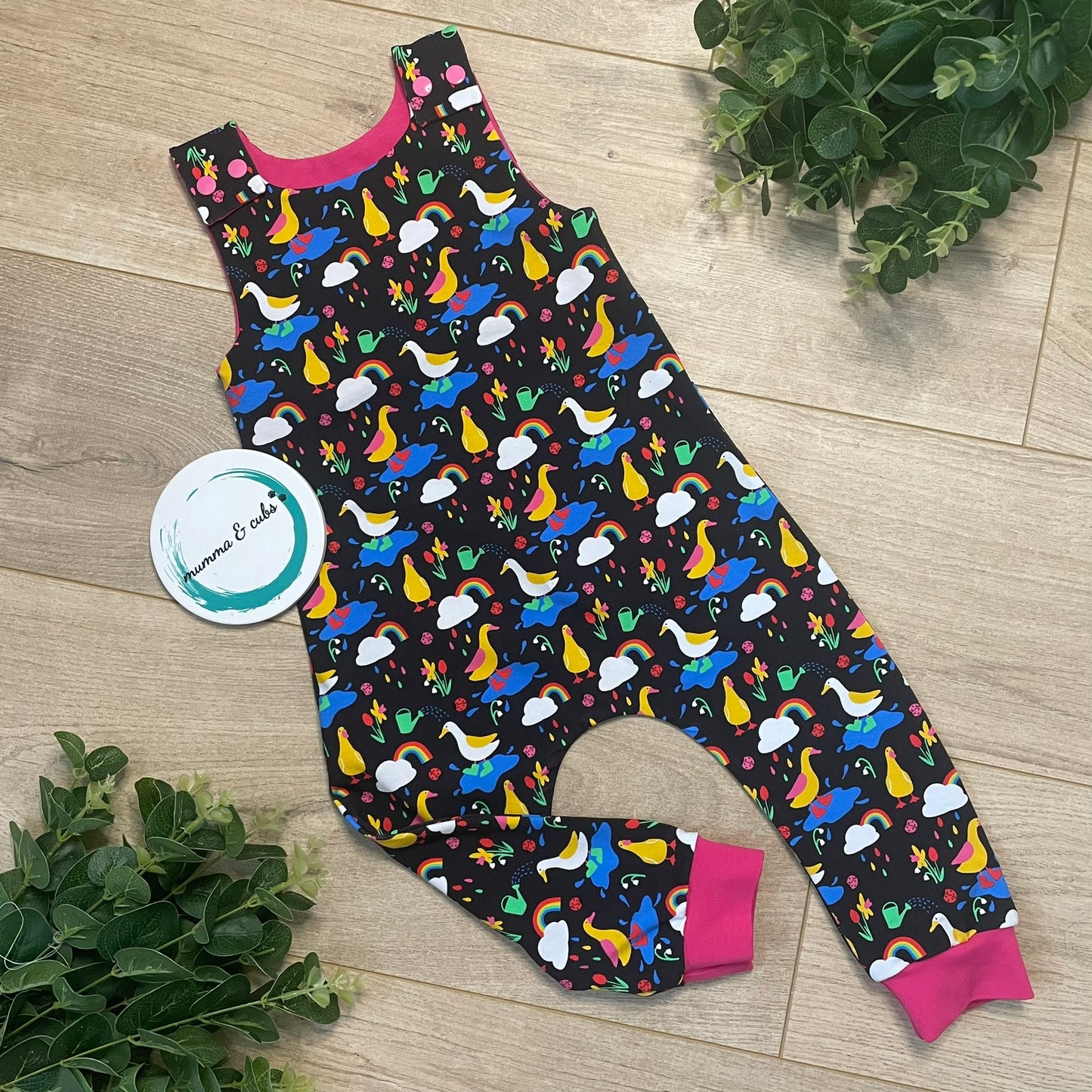 A pair of colorful dungarees for babies, with rainbows and ducks jumping in puddles