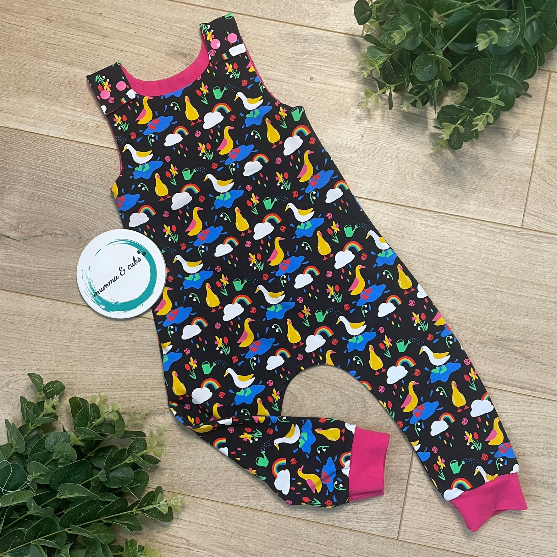A pair of colorful dungarees for babies, with rainbows and ducks jumping in puddles