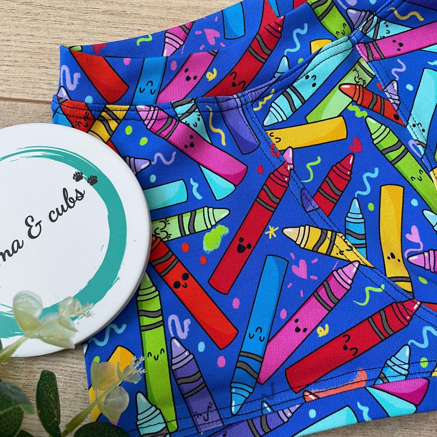 Colorful crayon-patterned boxers on a wooden surface with a plant in the corner.
