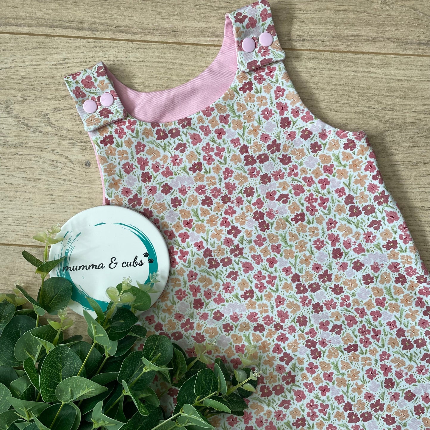 Pink Floral dress with pink lining on a wooden surface next to green leaves.